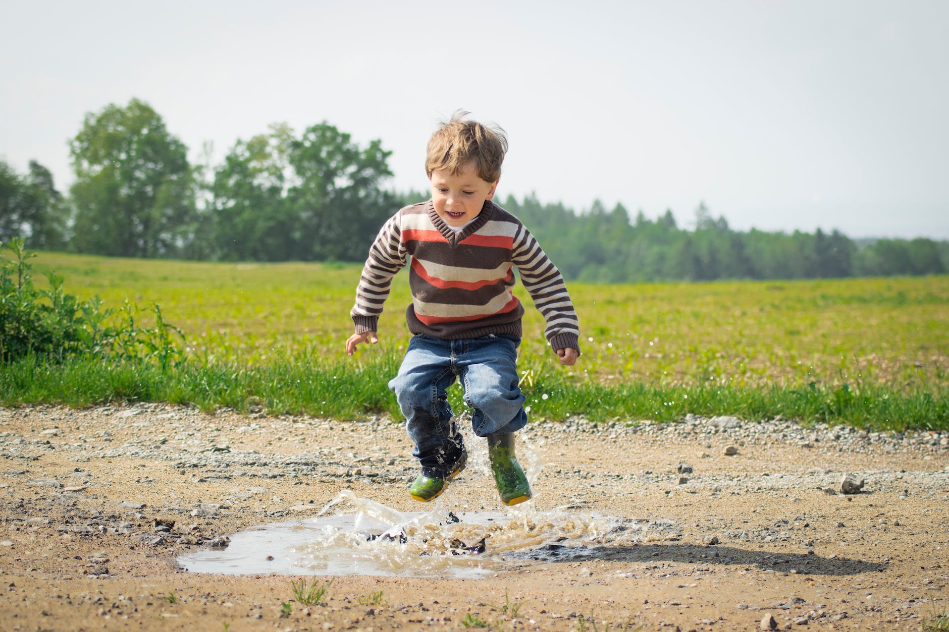 young male child joyously jumping into a puddle